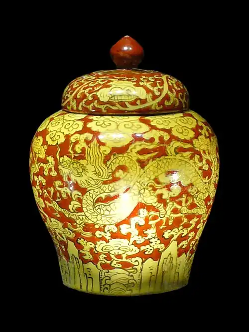 A porcelain jar with a red handle on top along with yellow dragons and clouds inscribed on a red background