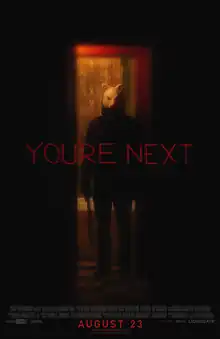 A figure wearing a fox mask stands in a doorway holding a machete by his side